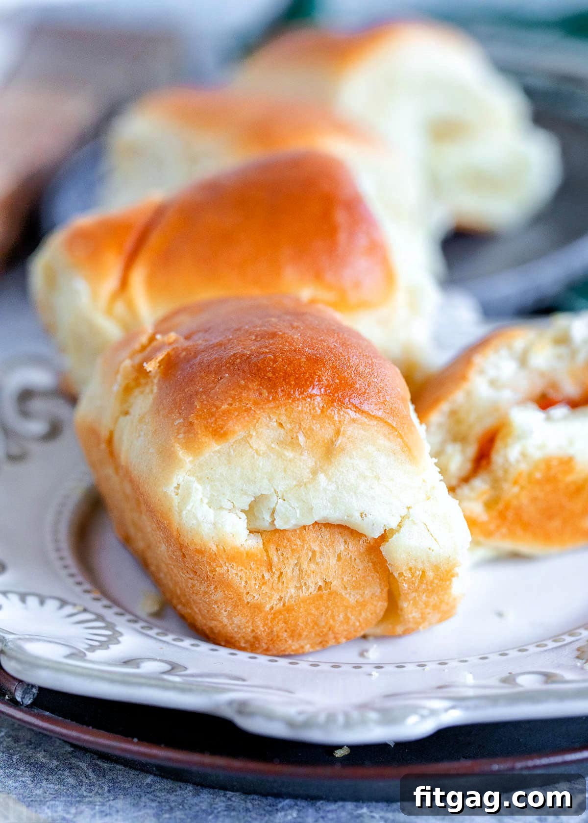 a couple rolls on a white plate with more rolls in background along with a roll that has butter and jelly and is half eaten.