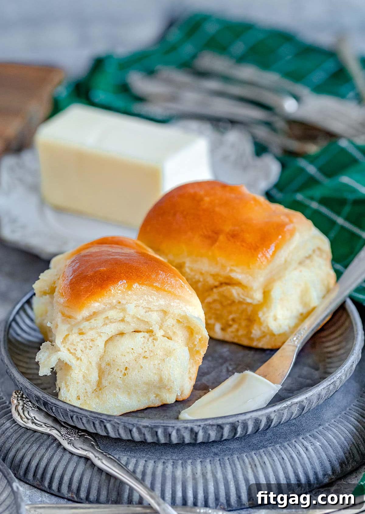two parker house rolls on a small metal plate with a stick of butter in the background.
