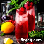 Shot of Cranberry Gin Cocktails on a dark surface, garnished with fresh mint and accompanied by lemons.