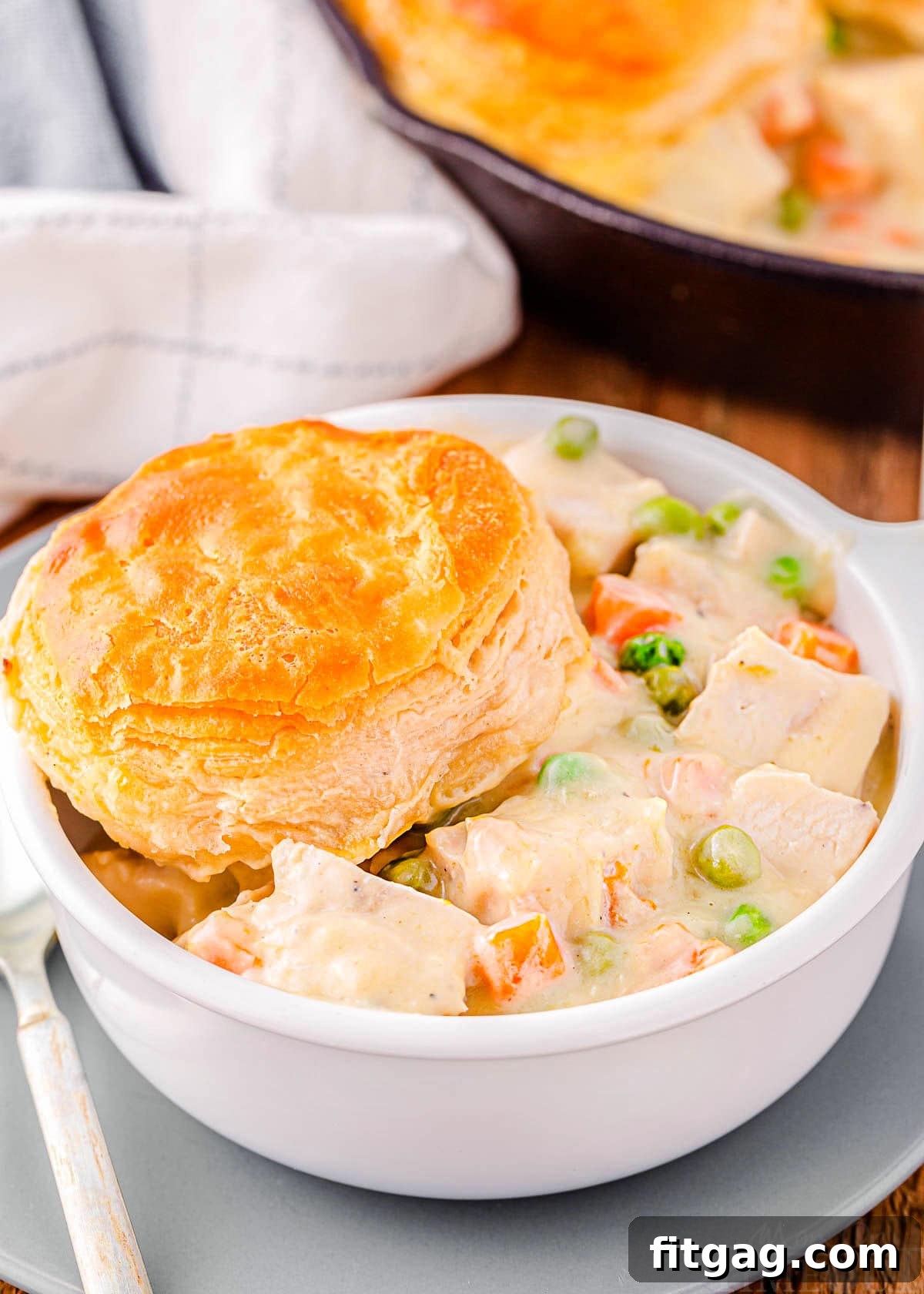 bowl filled with turkey pot pie and topped with a biscuit. the rest of the pot pie can be seen in the cast iron skillet in the background.