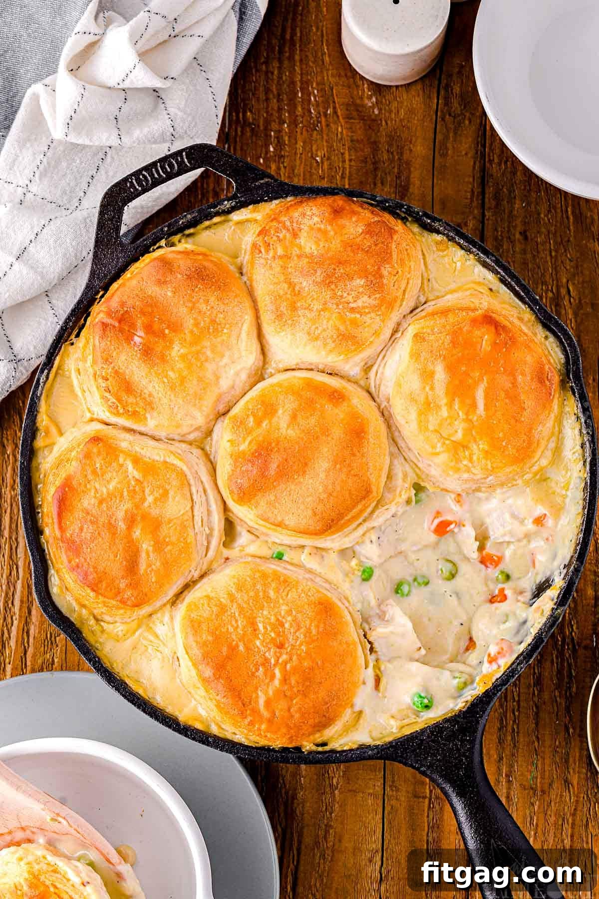 top down look at black cast iron skillet with one biscuit removed off the turkey pot pie. skillet is sitting on a wood surface.