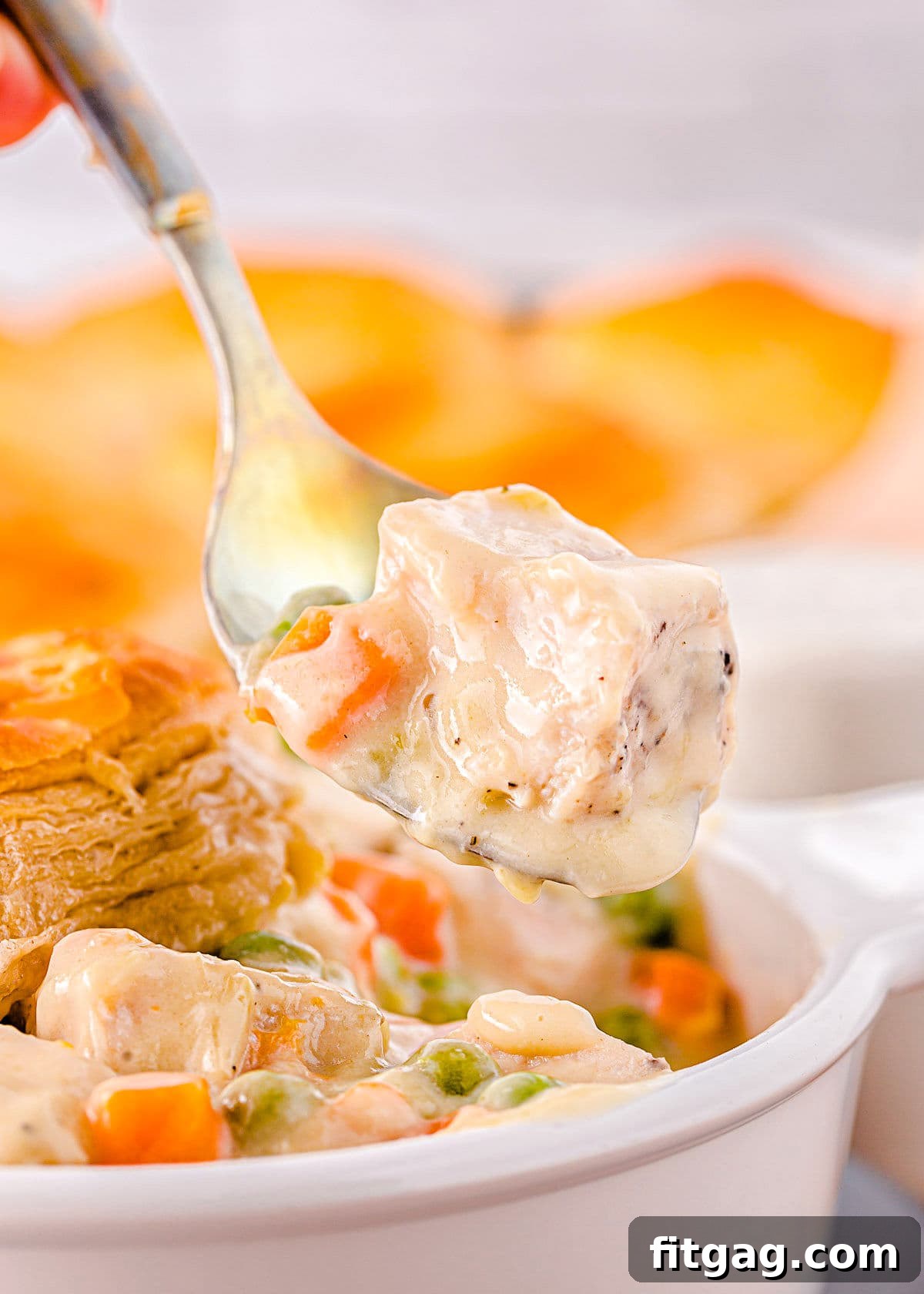 forkful of turkey pot pie being lifted out of a white bowl with biscuit topping seen in the background.