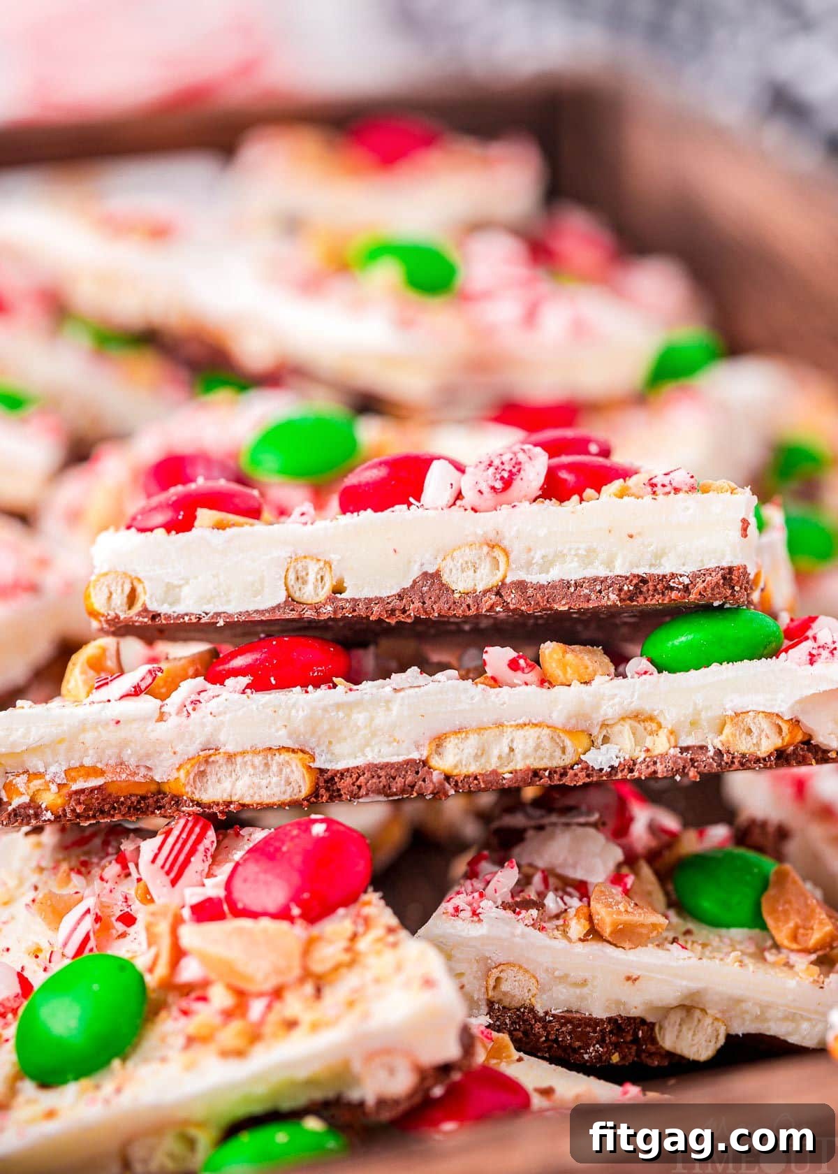 A top-down view of beautifully arranged pieces of festive Christmas Bark, layered in a shallow wooden tray, showcasing its colorful holiday decorations.