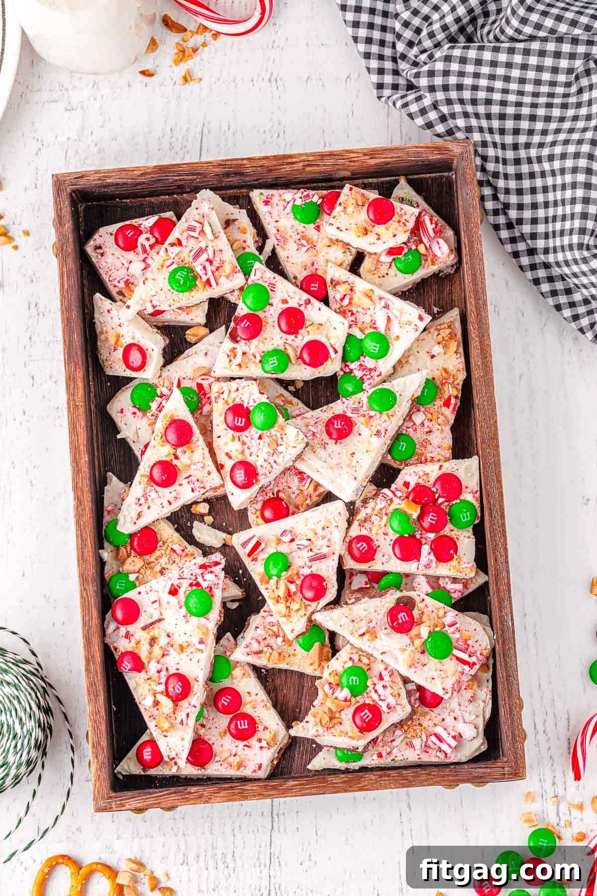 An inviting top-down shot of a generous quantity of Christmas-decorated chocolate bark, carefully placed in a rustic dark wooden tray, highlighting its rich textures and holiday toppings.