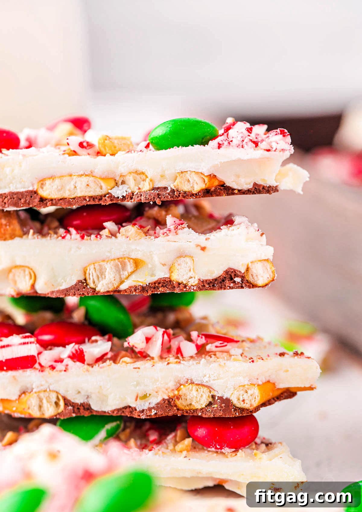 Four perfectly stacked pieces of festive Christmas bark, each adorned with a delightful mix of pretzels, colorful M&Ms, and crushed candy canes, ready to be enjoyed.