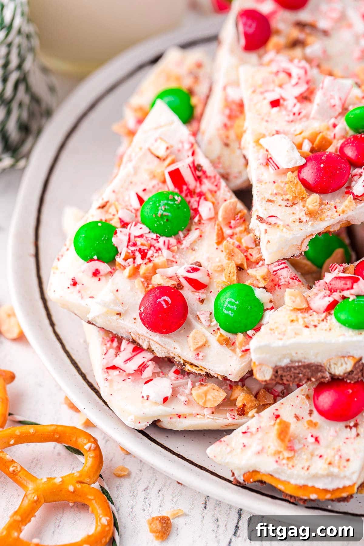 A delectable piece of Christmas candy bark resting on a pristine white plate, showcasing its beautiful festive decorations and crunchy pretzel base.