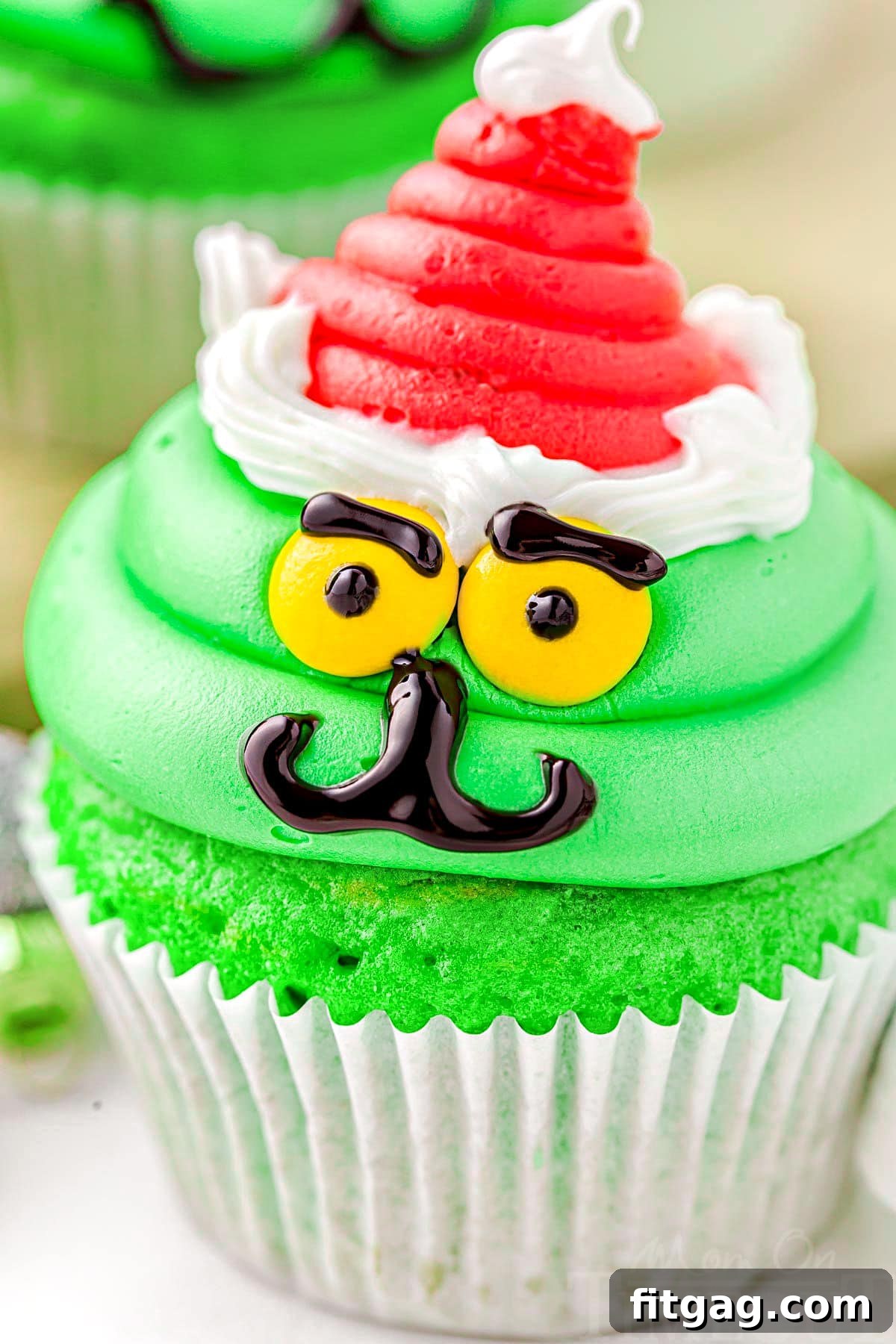 close up look at grinch decorated cupcake complete with santa hat. bright green frosting and cupcake.
