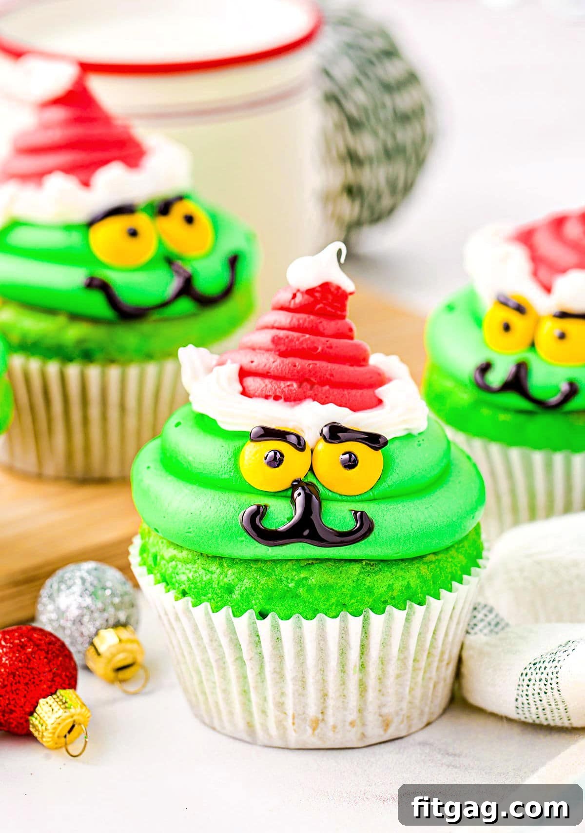 christmas cupcakes decorated like the grinch with red santa hat.