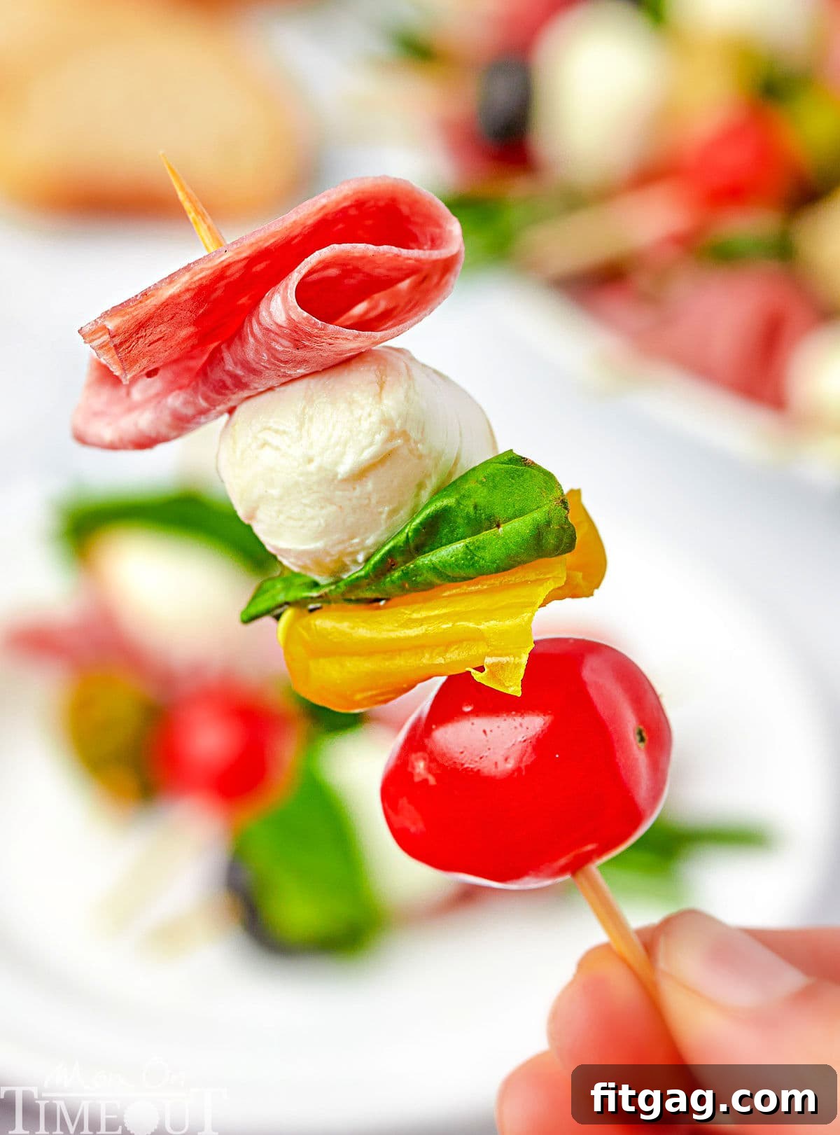 one antipasto skewer being held up over a plate.