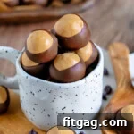A bunch of buckeye candy filled up a white mug sitting on a white marble surface. more buckeyes can be seen in the background.