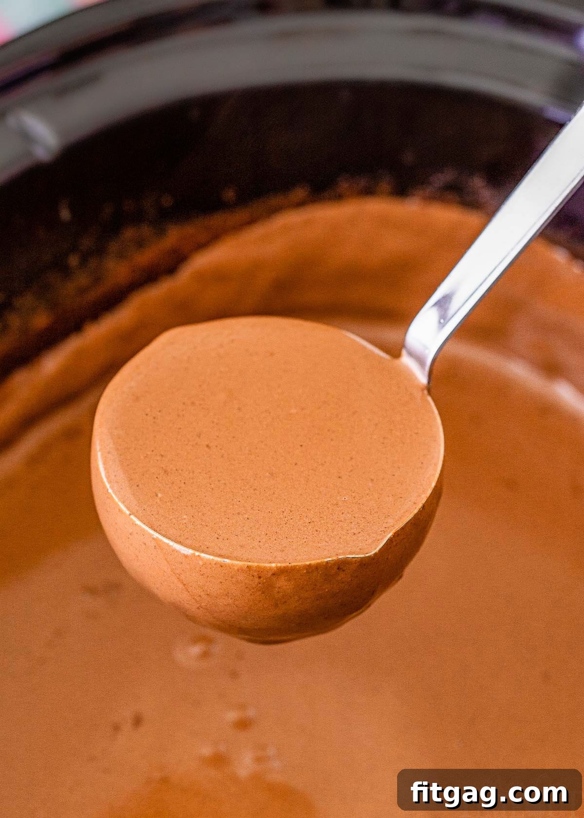 A ladle scooping out rich, dark hot chocolate from a slow cooker, illustrating the creamy texture.