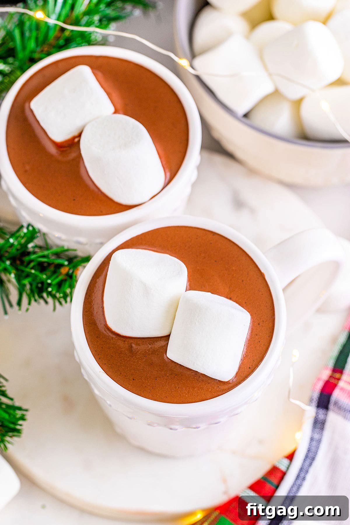 A top-down shot of two mugs of hot chocolate, garnished with marshmallows, placed beside a bowl of jumbo marshmallows, ready for indulgence.