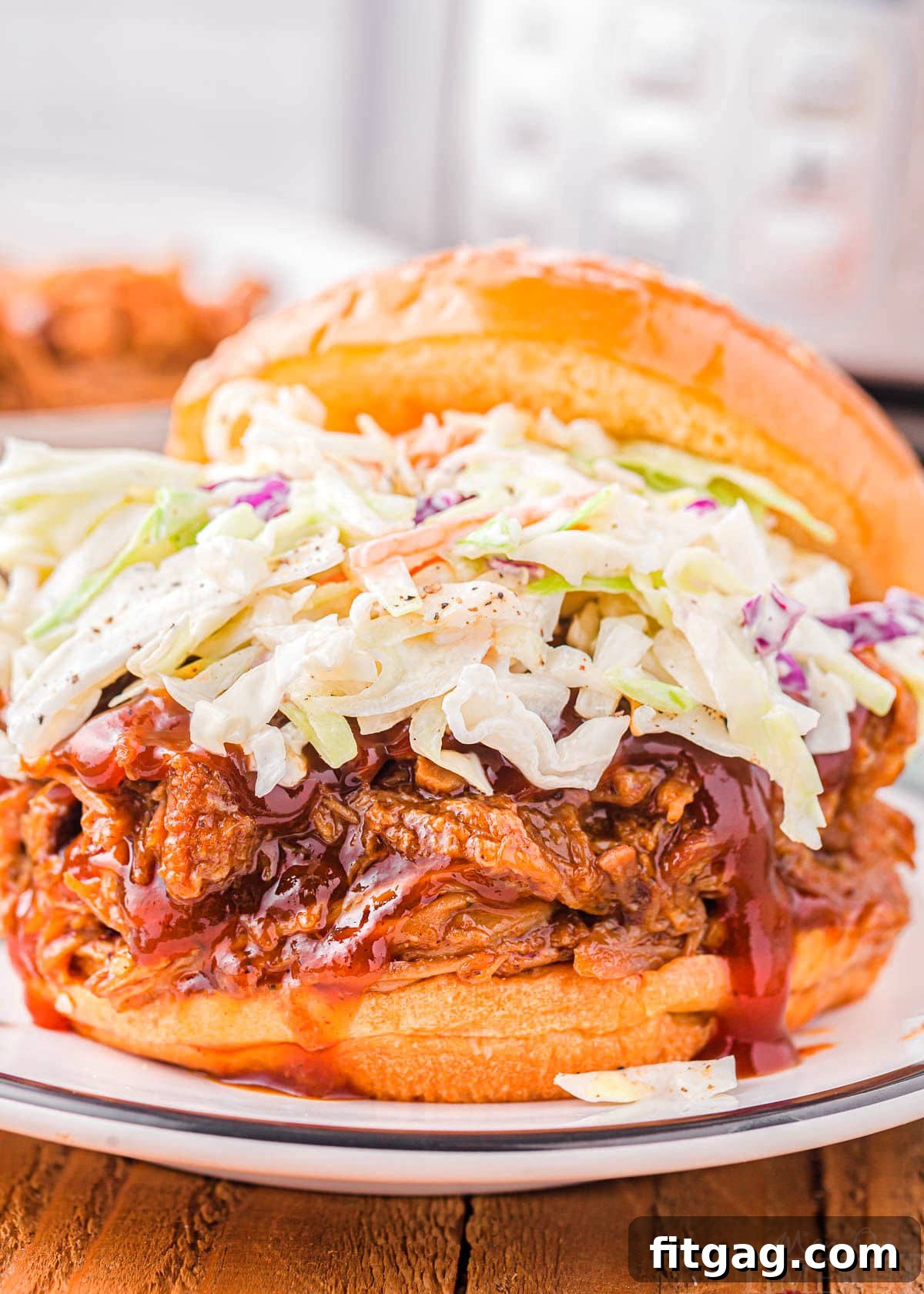 Effortless Instant Pot Pulled Pork 4 A delicious pulled pork sandwich topped with creamy coleslaw on a white plate, with an Instant Pot softly blurred in the background.