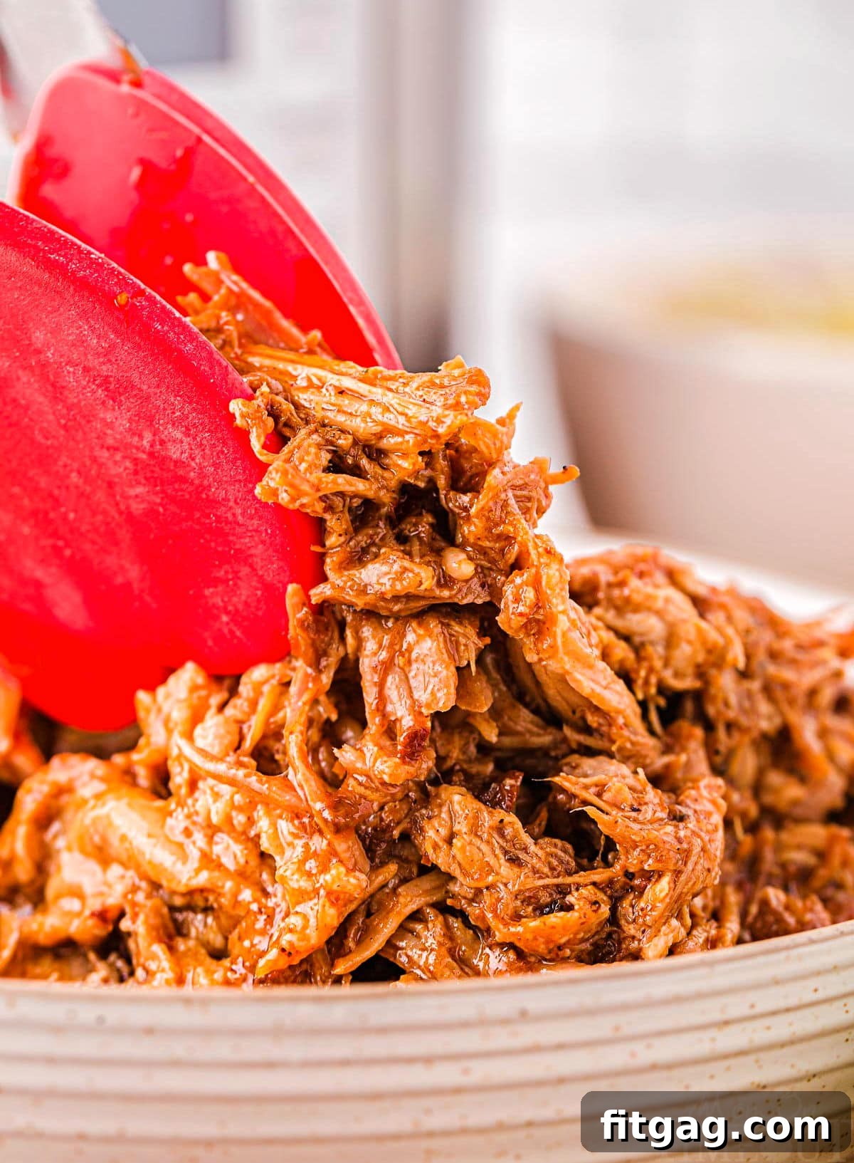 A pair of red tongs expertly holding up a generous portion of shredded Instant Pot pulled pork, highlighting its perfectly tender texture.