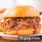 A delicious Instant Pot pulled pork sandwich sits on a plate, with an Instant Pot in the background.