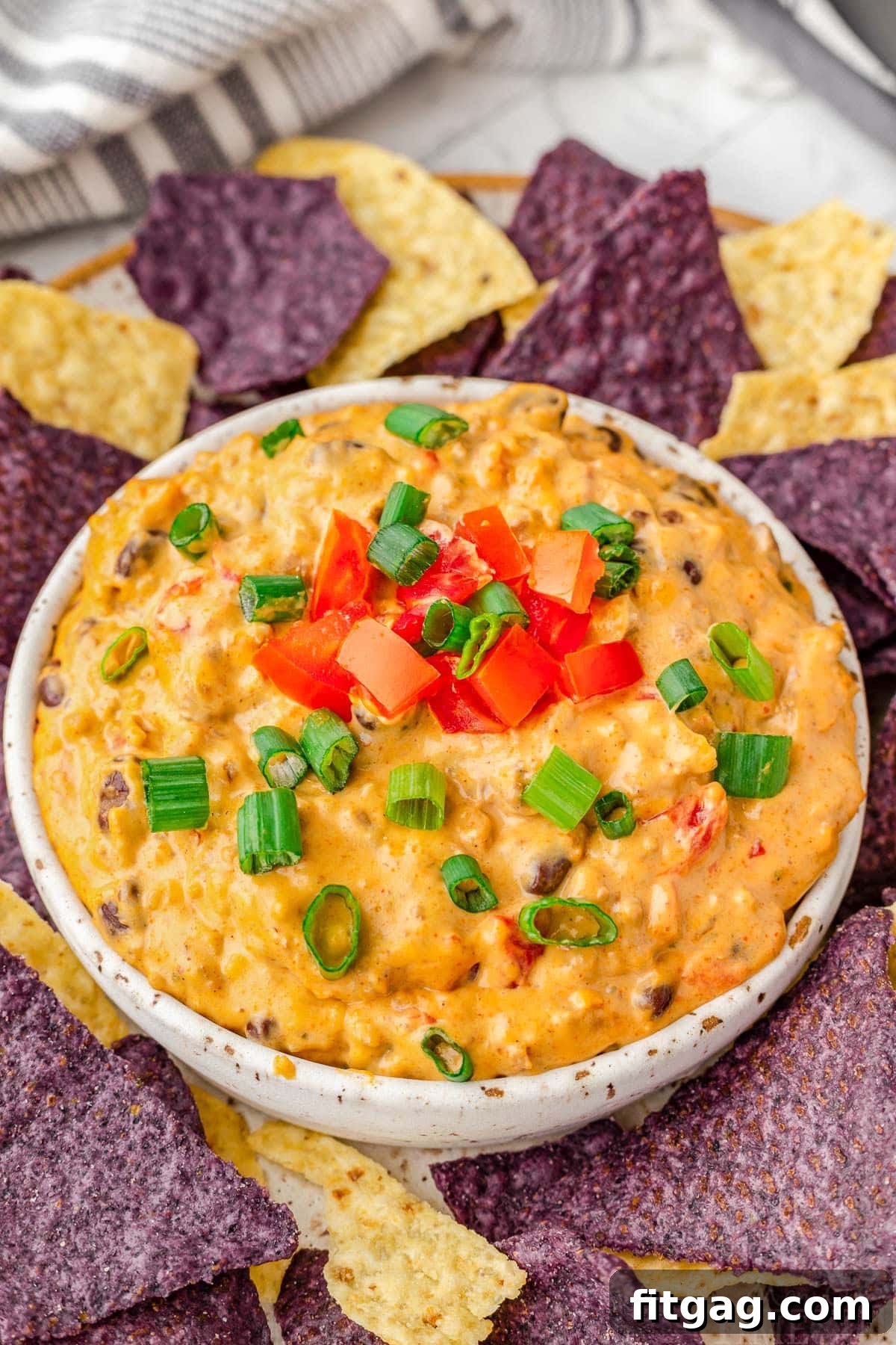 Irresistible Rotel Dip 2 medium white bowl filled with rotel dip and topped with sliced green onions and diced tomatoes surrounded by blue and white corn tortilla chips.