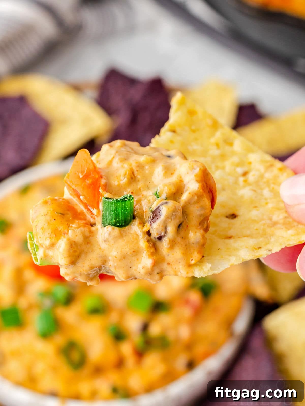 Irresistible Rotel Dip 3 rotel dip scooped onto a tortilla chip held over a bowl of the dip.