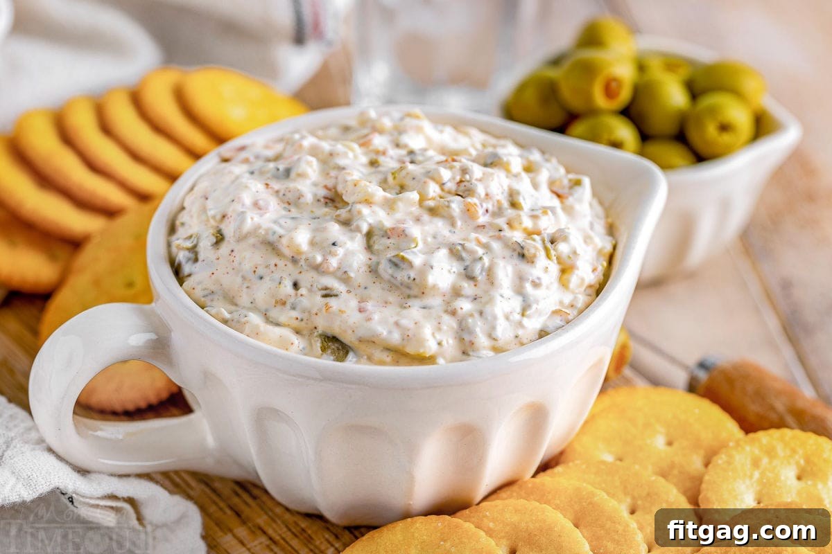 Rich Olive Spread 3 creamy olive dip in a white bowl with crackers surrounding it. a small white bowl with olives can be seen in the background.