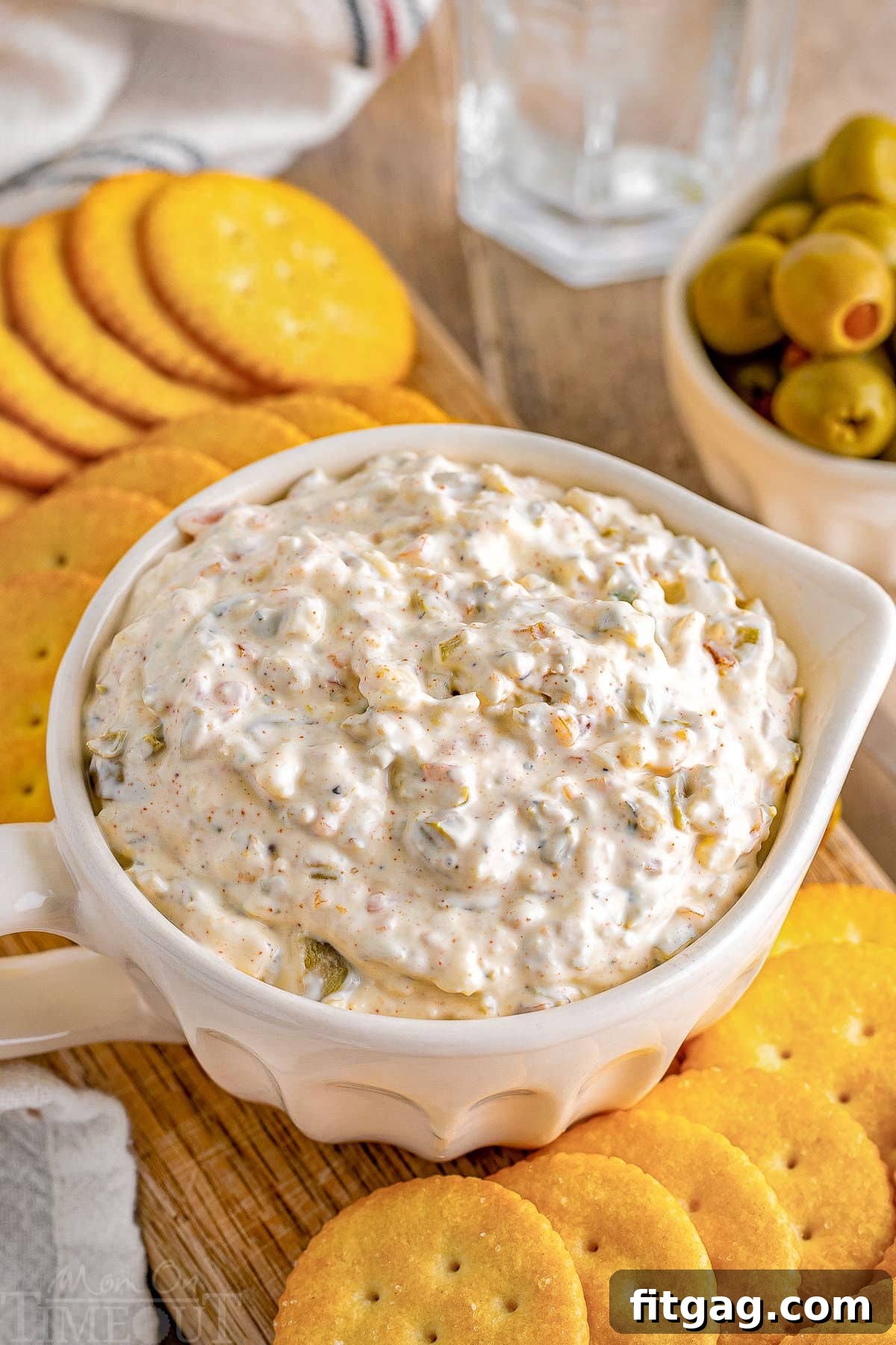 Rich Olive Spread 5 Top down angled view of green olive dip in a white bowl with a handle. Ritz crackers are on a board next to the dip.