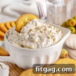 Rich Olive Spread 6 Olive dip in a small white bowl sitting on a wood board surrounded by crackers and a small bowl of green olives sitting off to the side. Glass of water in the background.