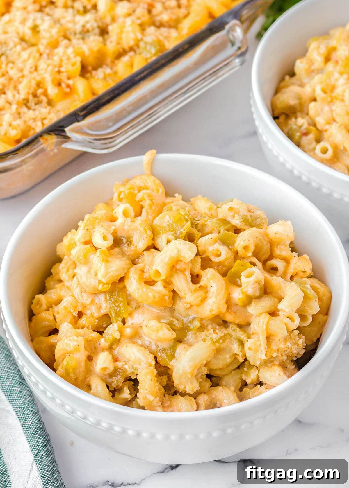 mac and cheese in a white bowl sitting on a marble surface. casserole dish and another bowl can be seen in the background.
