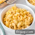 mac and cheese in a white bowl sitting on a marble surface. casserole dish and another bowl can be seen in the background.