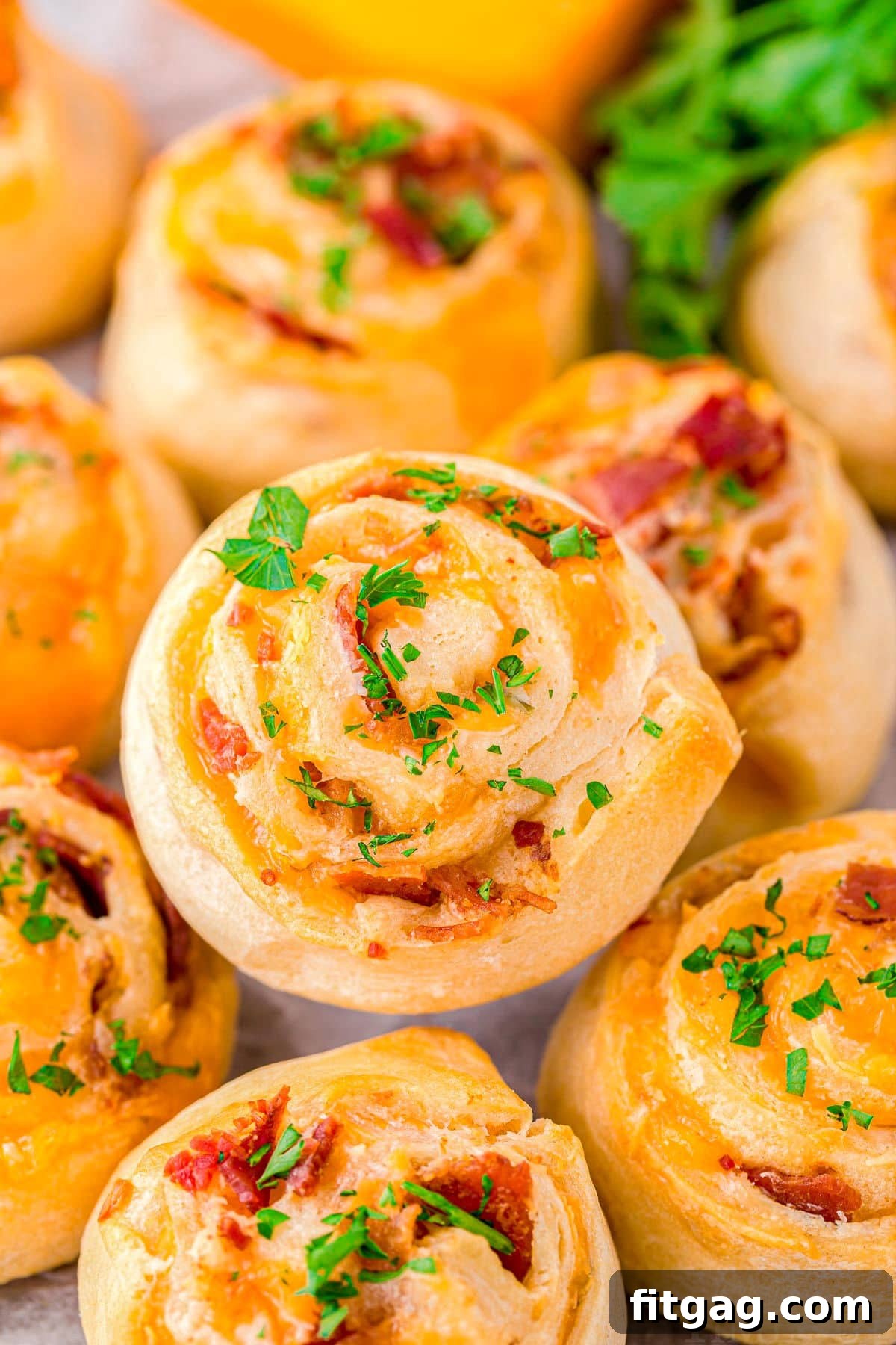 Cheesy Bacon Pinwheel Bites 2 Delicious Cheddar Bacon Pinwheels stacked on a plate, garnished with fresh chopped parsley, ready to be served as an appetizer.