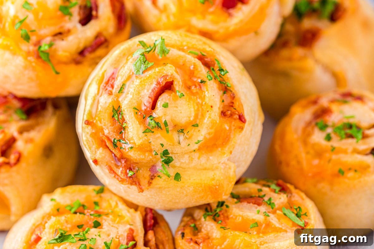 Cheesy Bacon Pinwheel Bites 5 Freshly baked Cheddar Bacon Pinwheels piled high on a white plate, garnished with fresh parsley, ready to be enjoyed as a perfect snack or appetizer.
