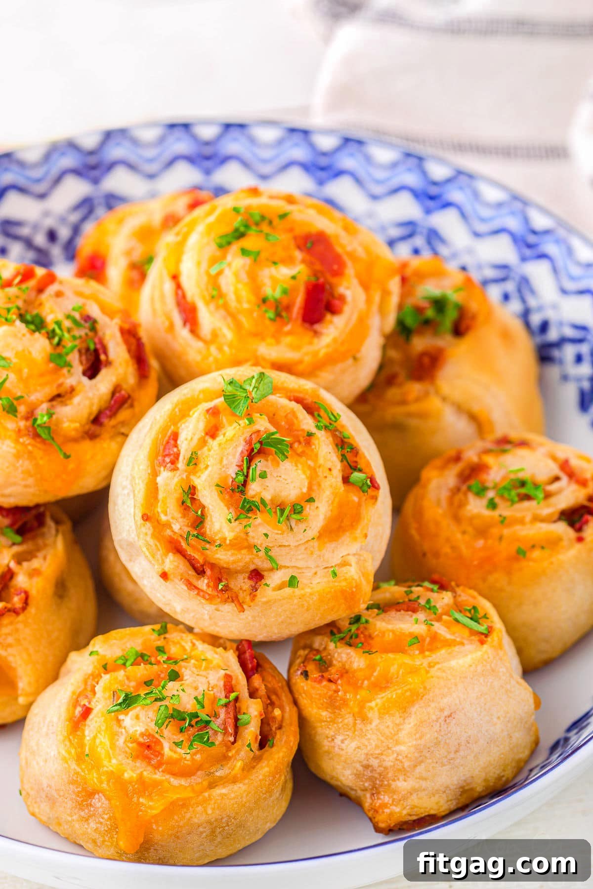 Cheesy Bacon Pinwheel Bites 6 A vibrant blue and white bowl filled with golden Cheddar Bacon Pinwheel appetizers, perfectly baked and ready to be enjoyed at a gathering.