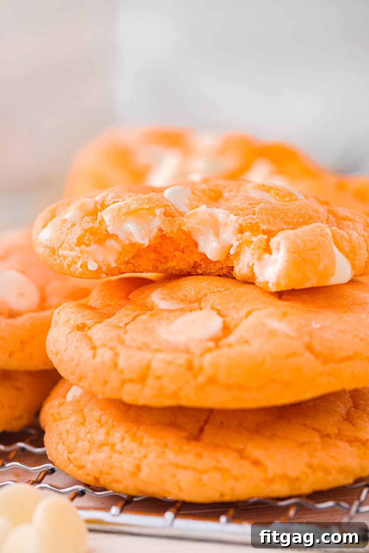 Three perfectly baked creamsicle cookies stacked artfully, with the top cookie having a delicious bite taken out, revealing its soft, chewy interior.