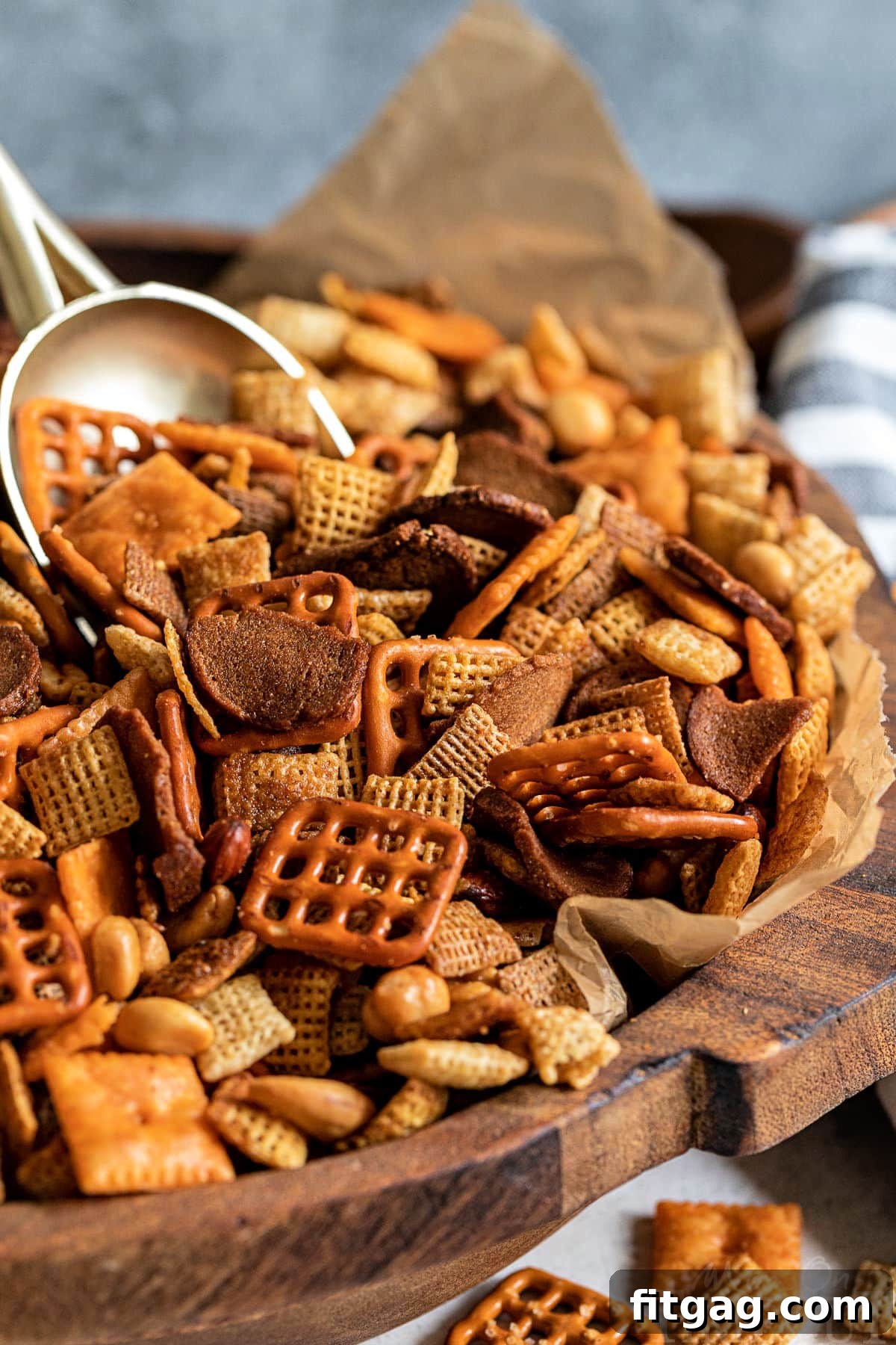 A large wooden bowl filled with golden-brown homemade Chex Mix, featuring a prominent gold scoop, ready for serving.