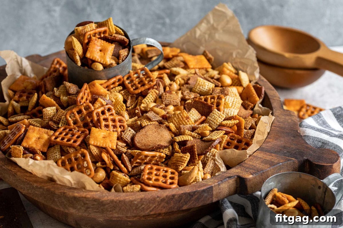 A large wooden bowl brimming with Chex Mix, with a metal cup nestled inside, ready to scoop out the crunchy snack.