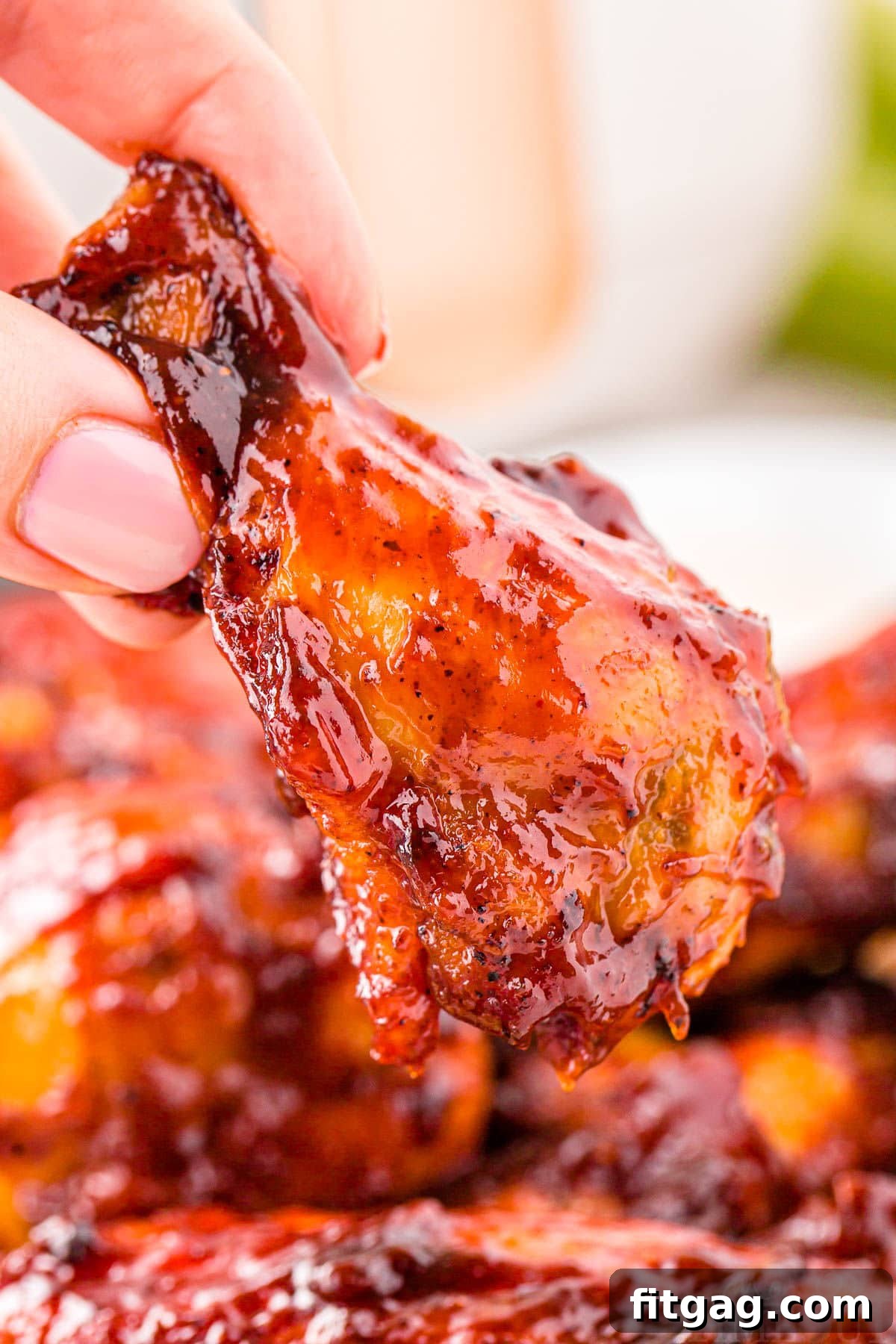 A hand holding a perfectly cooked BBQ Air Fryer Chicken Wing, crispy and brushed with barbecue sauce.
