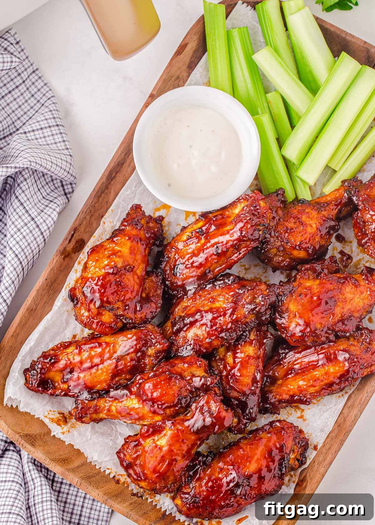 Top-down view of BBQ chicken wings arranged on a wooden board, accompanied by crisp celery sticks and creamy ranch dressing.