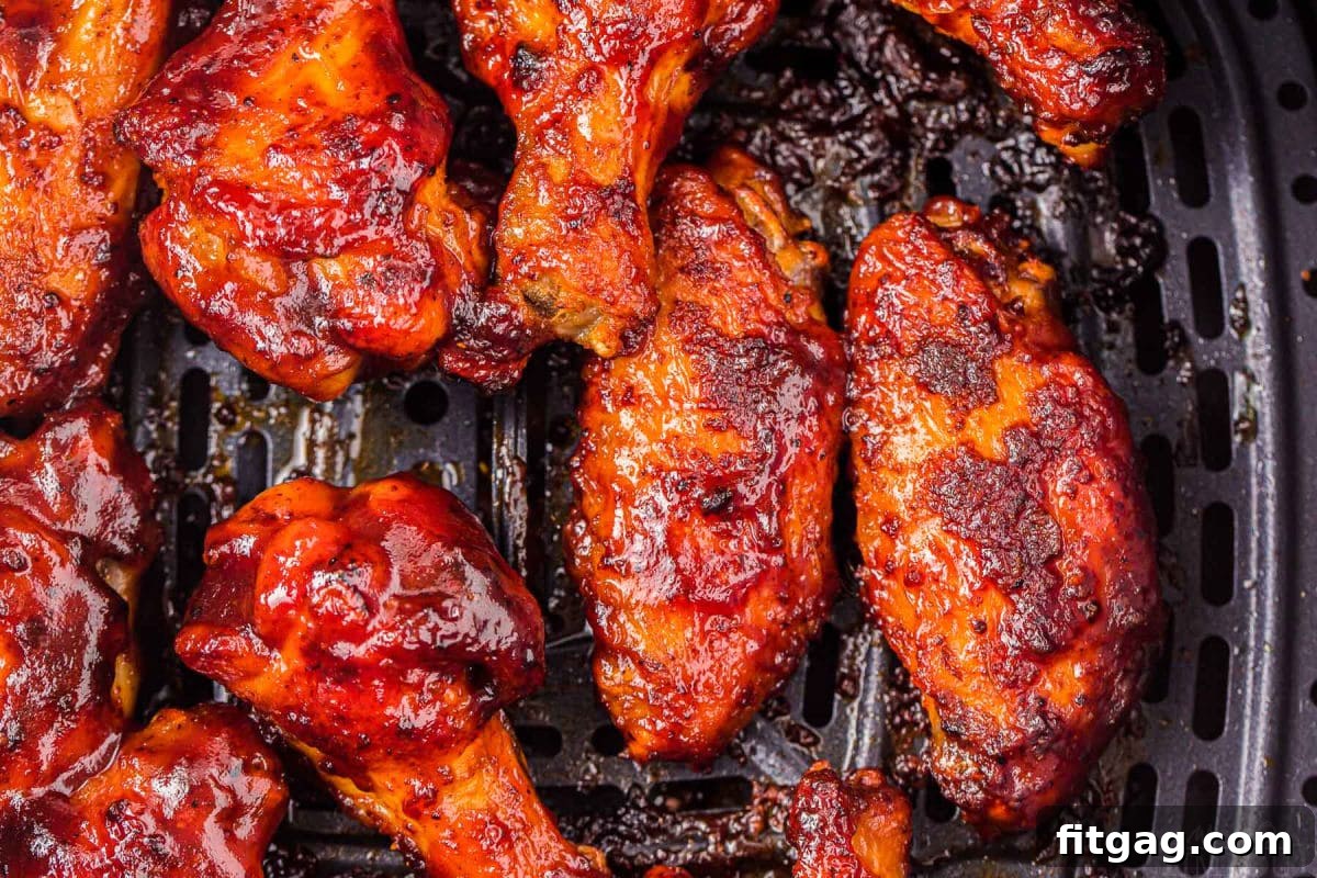 Close-up, top-down view of chicken wings cooking in an air fryer basket, beautifully brushed with barbecue sauce.