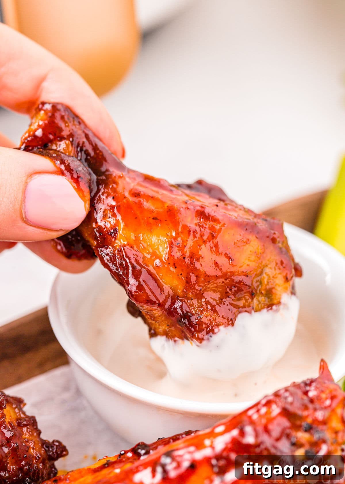 A BBQ air fryer chicken wing being dipped into a small bowl of creamy ranch dressing, highlighting its delicious crispness.