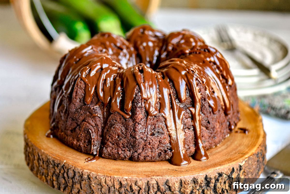 Decadent Chocolate Zucchini Cake 3 chocolate zucchini cake made in a bundt pan on wood cake stand with zucchinis in the background.