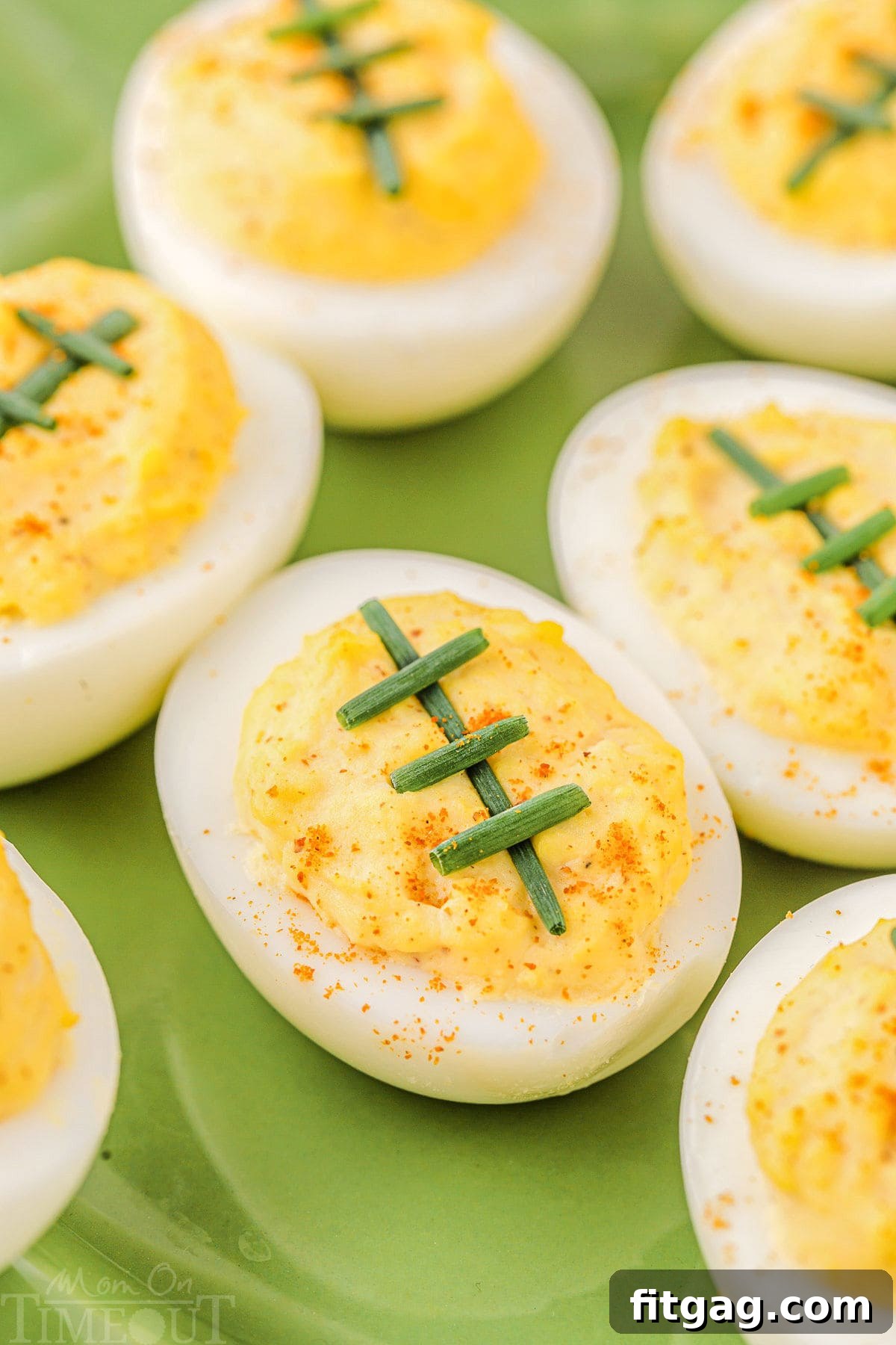 Green plate filled with deviled eggs decorated to resemble footballs, featuring chive laces. Perfect for a game day party.