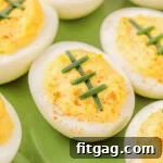 deviled eggs decorated to look like footballs with chives on a green plate.