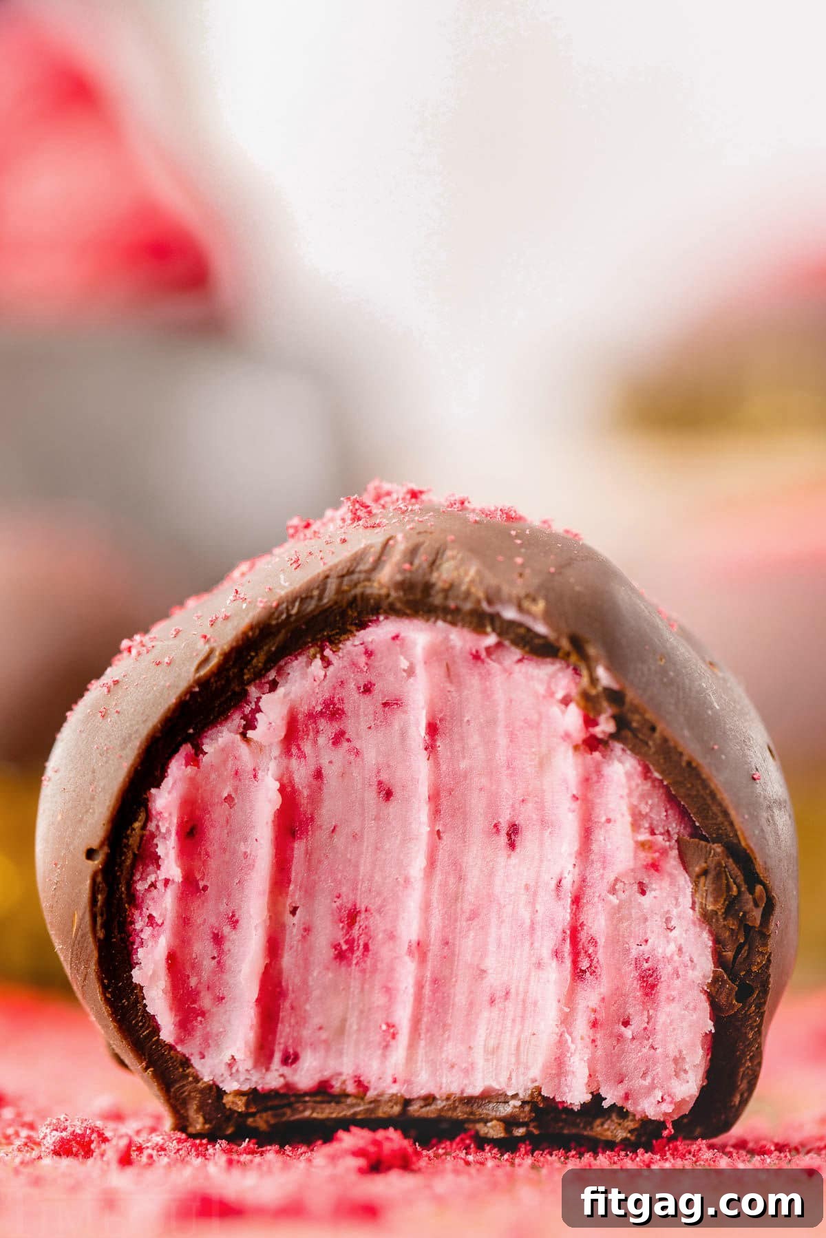 A close-up view of a single raspberry truffle, perfectly coated in dark chocolate. A small bite has been taken from it, revealing the bright, creamy, and seedless raspberry interior, showcasing the delightful contrast of textures and colors.