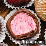 Close-up of a raspberry truffle covered in dark chocolate in a small paper liner next to more truffles.