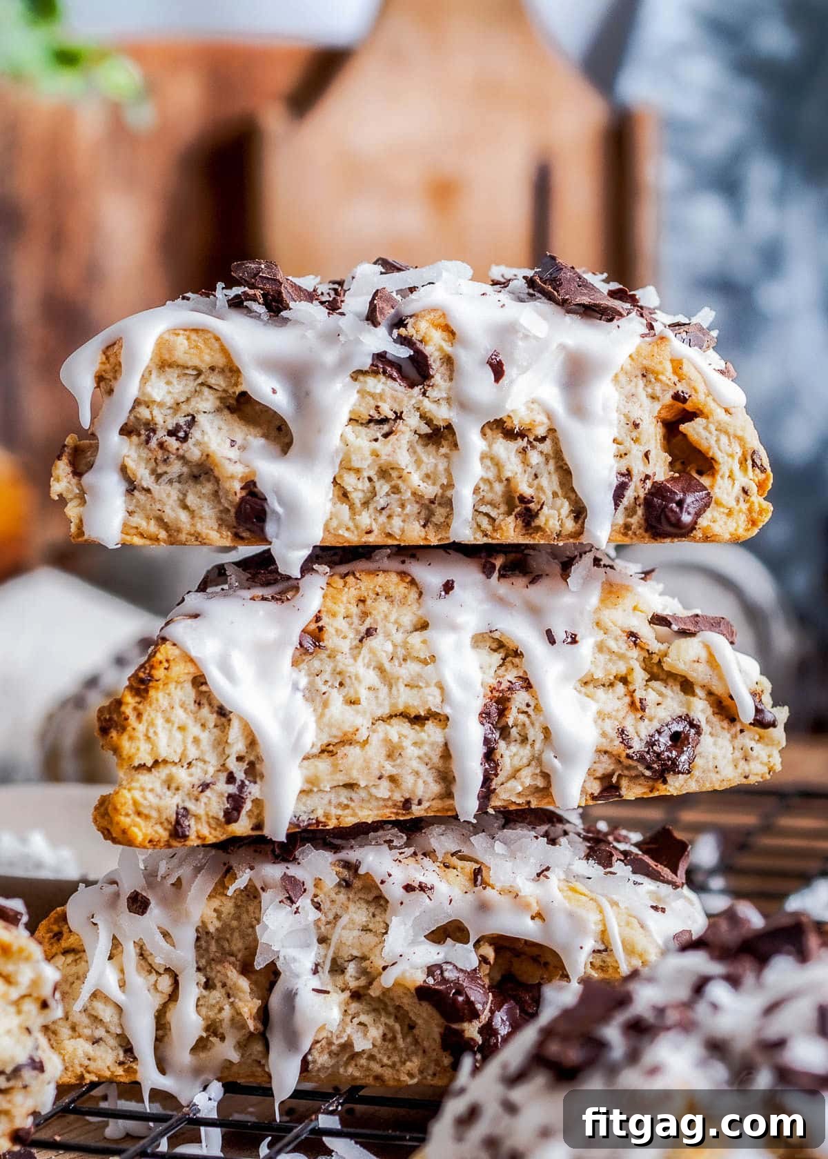 Three beautifully iced chocolate coconut scones, inspired by Almond Joy, stacked artfully on a rustic wooden board. The image highlights their rich texture and appealing presentation.
