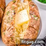 air fryer baked potato on a white plate topped with butter, salt and pepper. Freshly chopped green chives are in a small white bowl in the background.