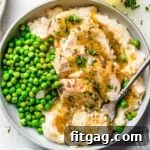 top down look at instant pot chicken breast sliced sitting on a bed of mashed potatoes with gravy over the top. green peas are also on the plate.