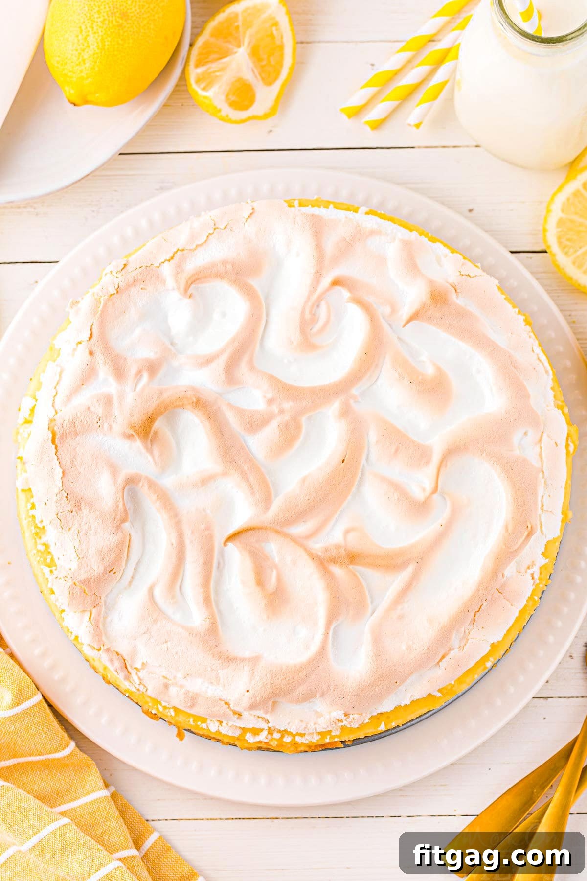 Top-down view of a whole lemon meringue cheesecake with golden-brown swirled meringue topping, garnished with fresh lemon slices.
