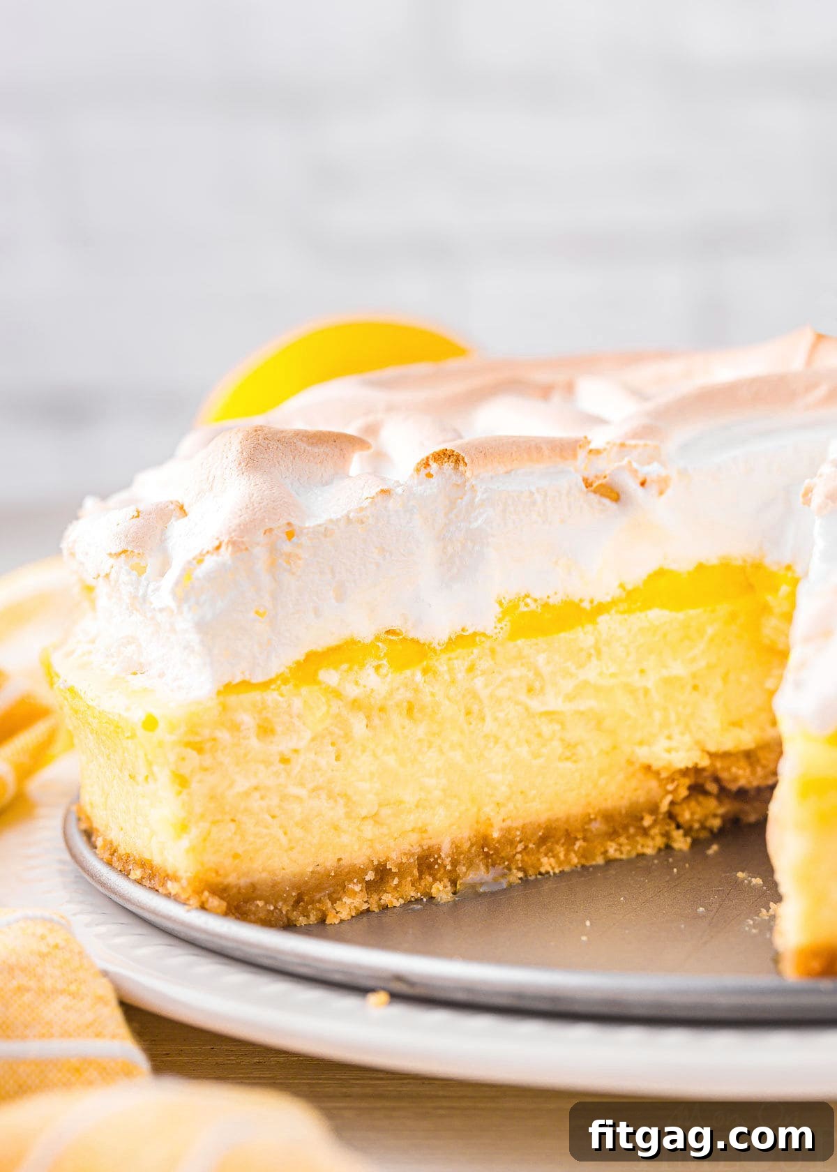 A whole lemon meringue cheesecake with a slice removed, sitting next to a yellow napkin.