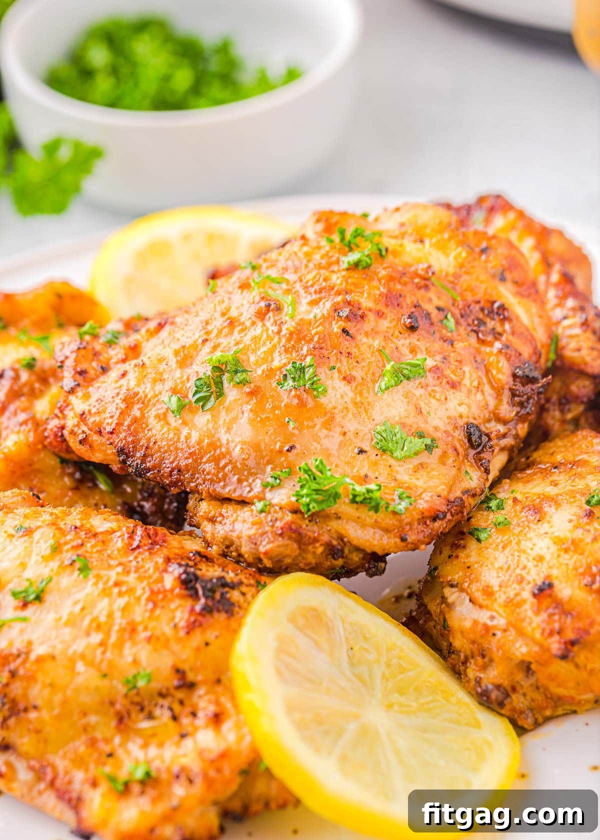 Four air-fried chicken thighs, golden brown and crispy, arranged on a white plate with fresh parsley and lemon slices for garnish. A perfect and inviting meal.