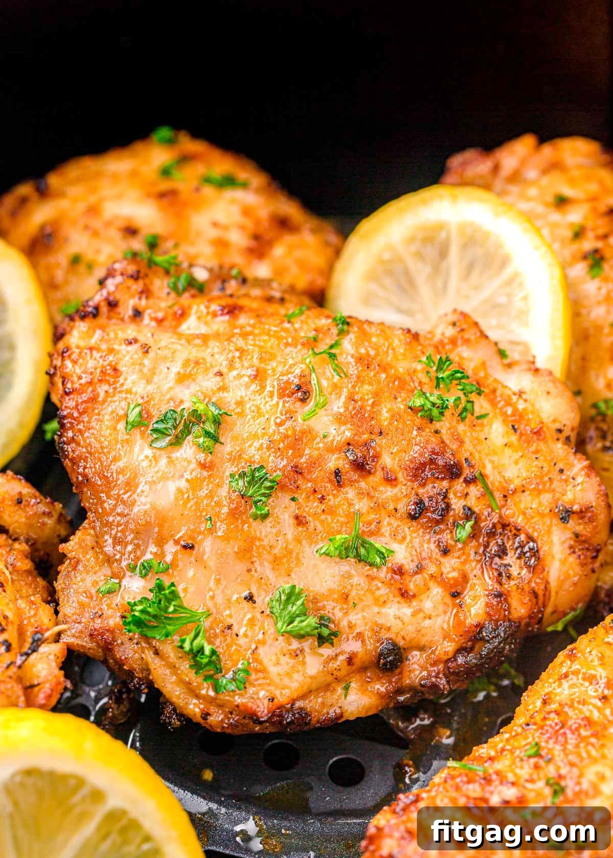 chicken thigh in air fryer cooked until golden brown, topped with parsley and lemon slices.