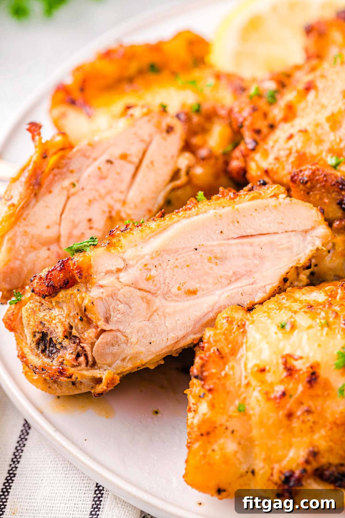 chicken thighs made in the air fryer on a white plate. One chicken thigh is cut in half so you can see the juicy meat.