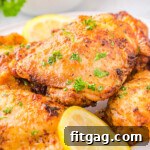 Four chicken thighs cooked in air fryer piled on a white plate and garnished with fresh parsley and lemon slices.